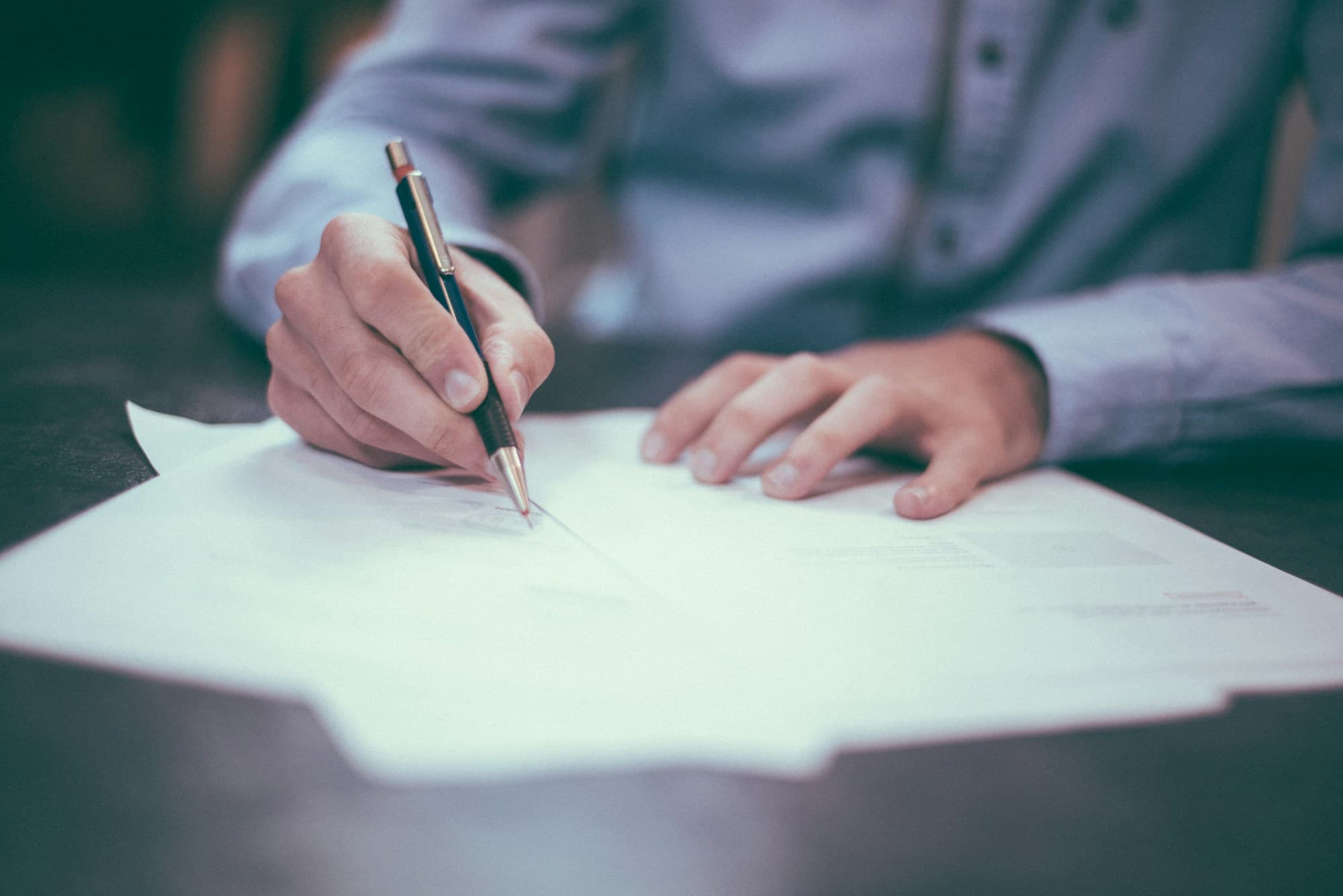 Hand signing a typed document on a wooden desk — the deliberative act of director and officer execution.