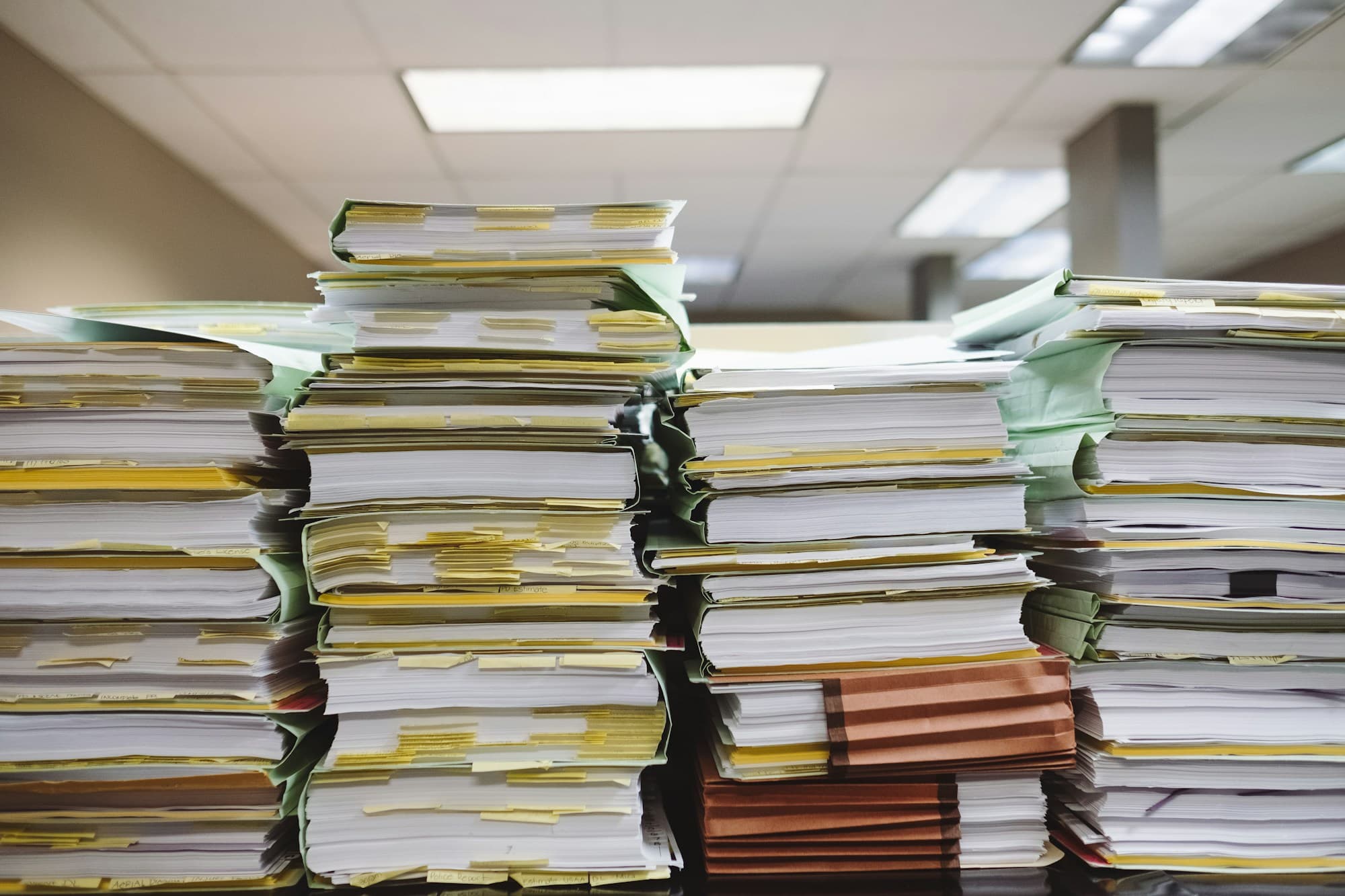 Top-down view of stacked paper documents and file folders — the working surface of a brokerage placement file.